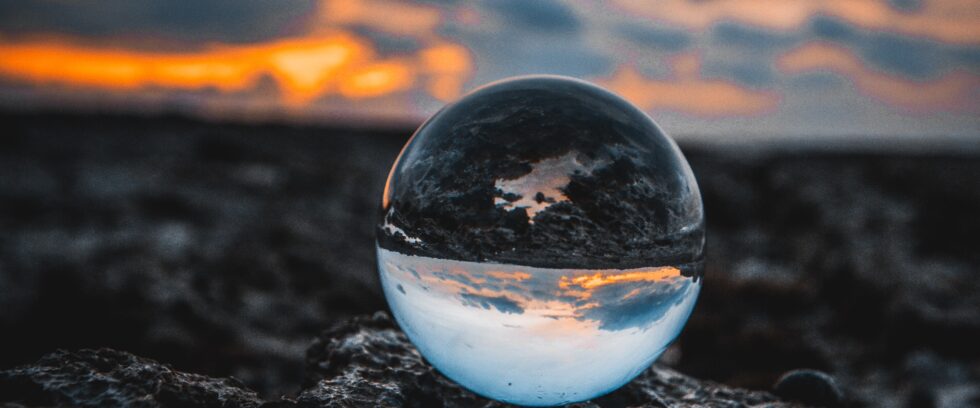 A crystal ball on a mountainside. The sunset in the distance is reflected upside down in the crystal ball.